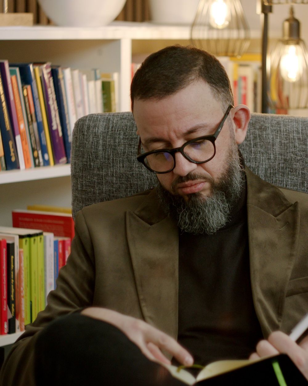 Chaker Cheniti liest in einem Sessel vor einem Bücherregal